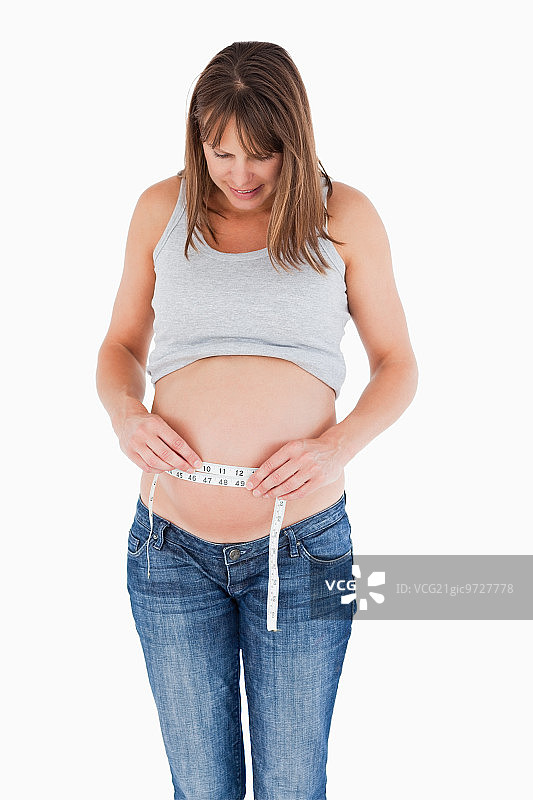 一个可爱的孕妇站在白色的背景下测量她的肚子图片素材