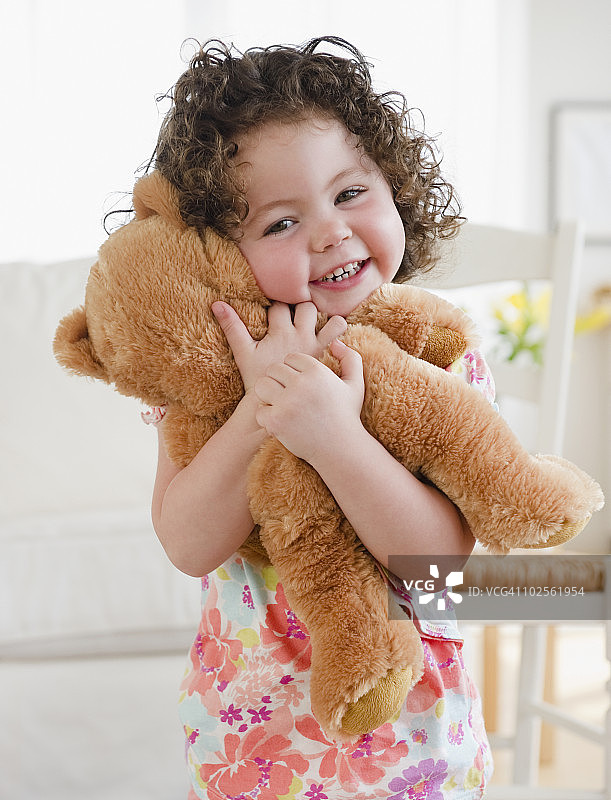 蹒跚学步的孩子抱着泰迪熊，微笑着图片素材