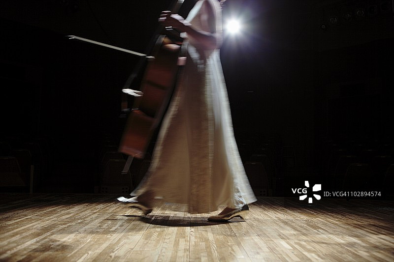 一个女大提琴手走在舞台上。图片素材