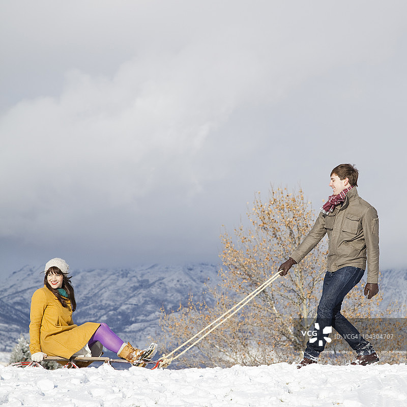一对年轻夫妇在雪地里拉雪橇图片素材