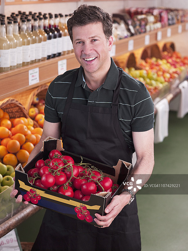 微笑的工人拿着西红柿在杂货店图片素材