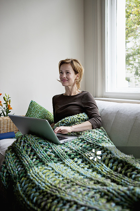 一个女人斜靠在沙发上使用笔记本电脑图片素材