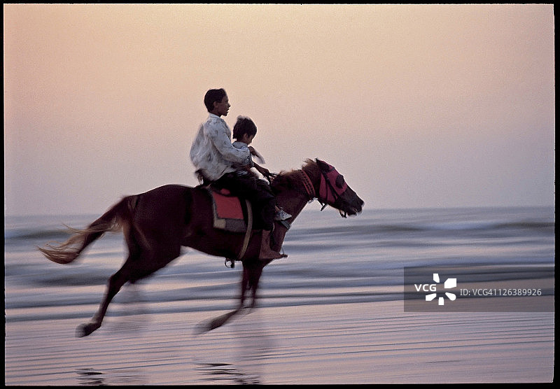 日落时海滩上骑马的人图片素材