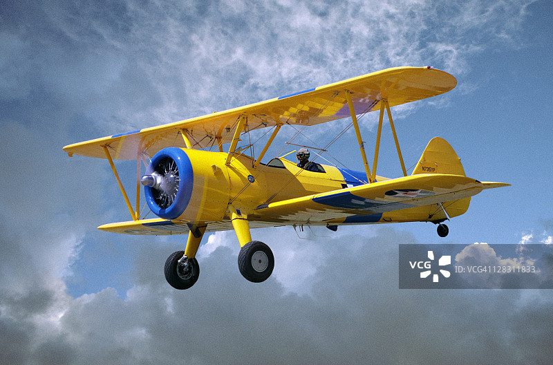 黄色硬脂人5YP双翼飞机在多云的天空中飞行图片素材