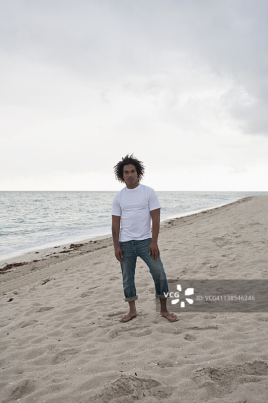 一个酷酷的年轻人站在沙滩上，正面图片素材