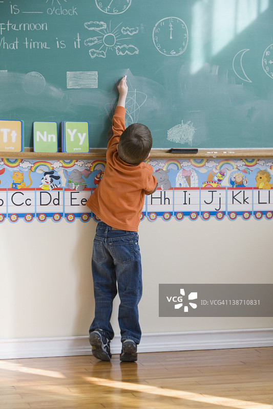 一个白人男孩在教室的黑板上画画图片素材