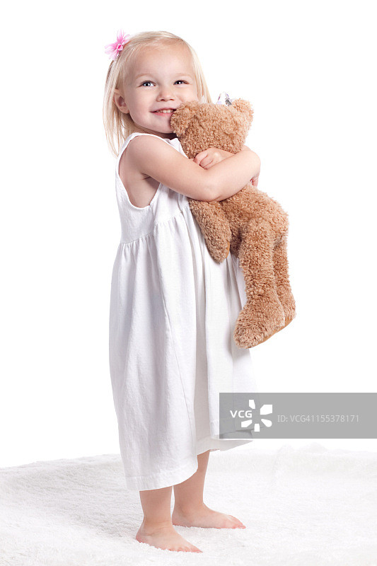 快乐的小女孩在白色连衣裙拥抱毛绒动物图片素材