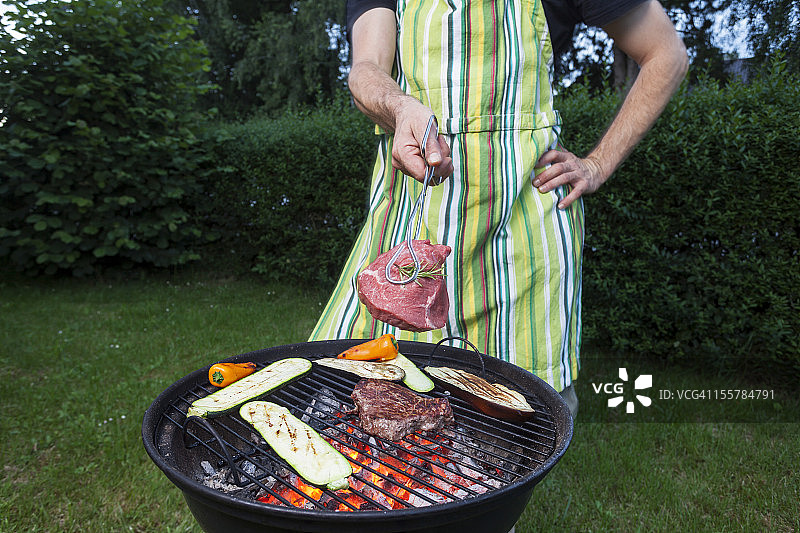 德国，成熟的男人拿着烤肉架上的肉图片素材