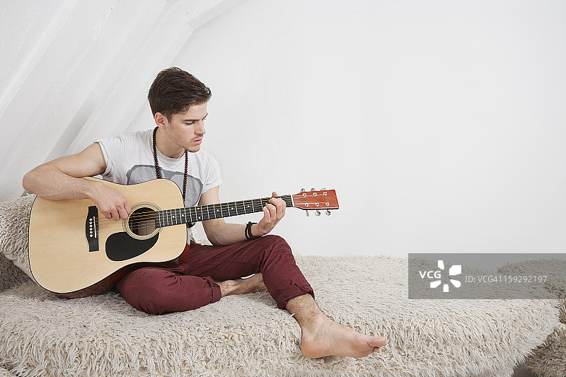 一个年轻人坐在皮草沙发上弹吉他图片素材