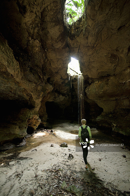 女人探索洞穴天花板瀑布。图片素材