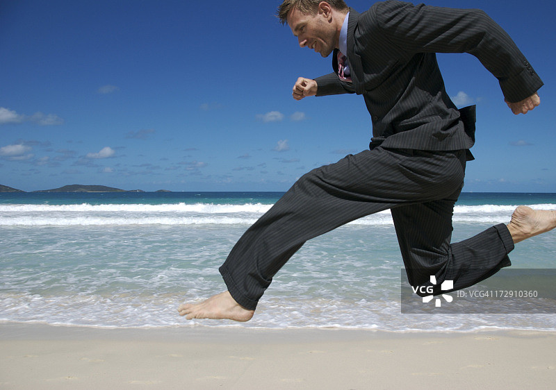 西装商人在热带海滩上赤脚跳跃图片素材