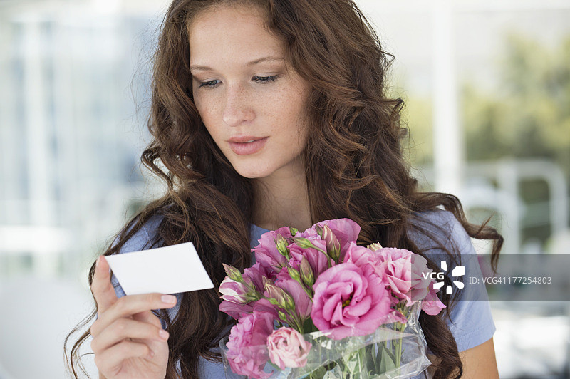一个女人正在读一张卡片，上面有一束鲜花图片素材