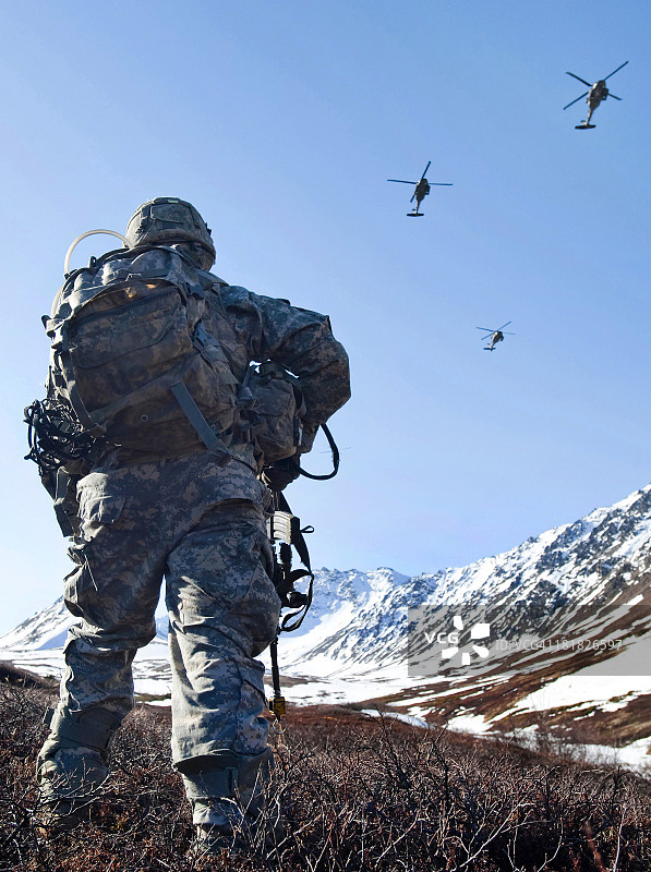 当UH-60黑鹰直升机在上空飞行时，士兵在阿拉斯加的丘格什山脉巡逻。图片素材