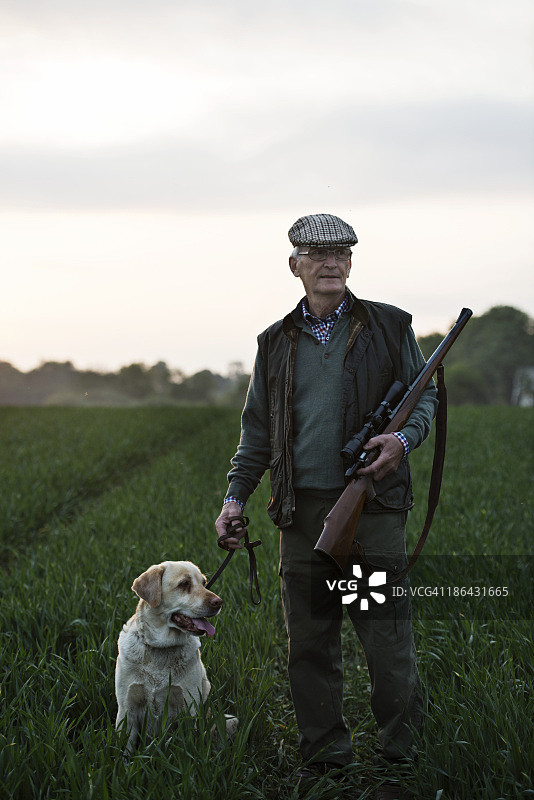 一个人带着狗和步枪站在田野里图片素材