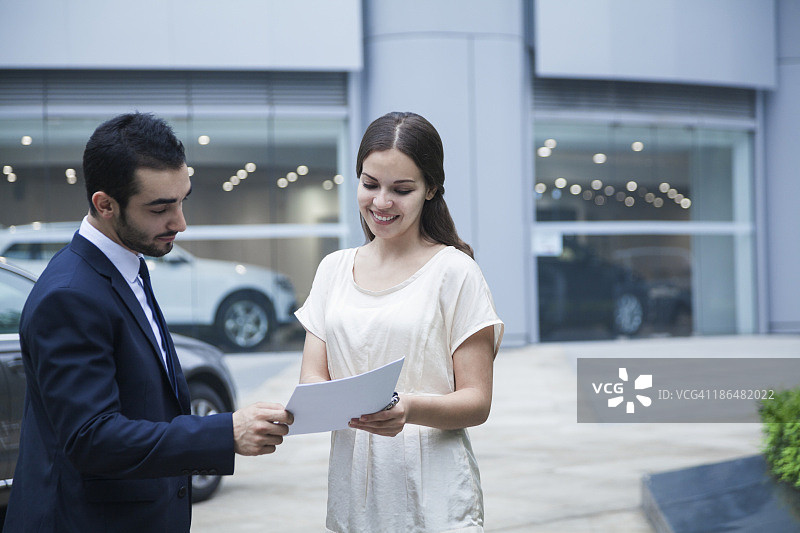 汽车推销员和一个年轻女子在一家汽车经销店看文件图片素材