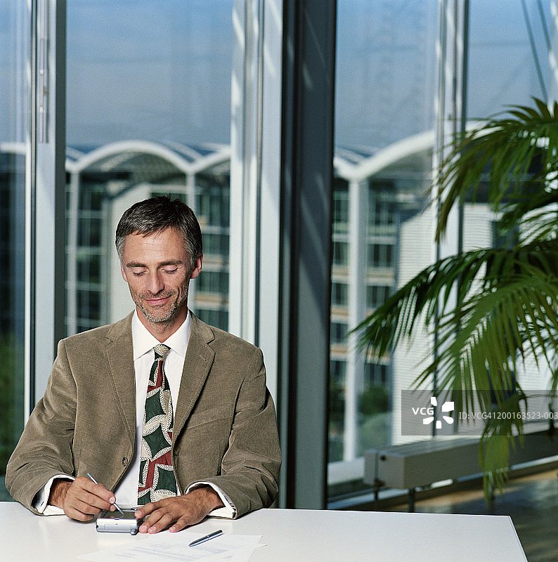 成熟的商人使用电子记事本坐在办公室的办公桌前图片素材
