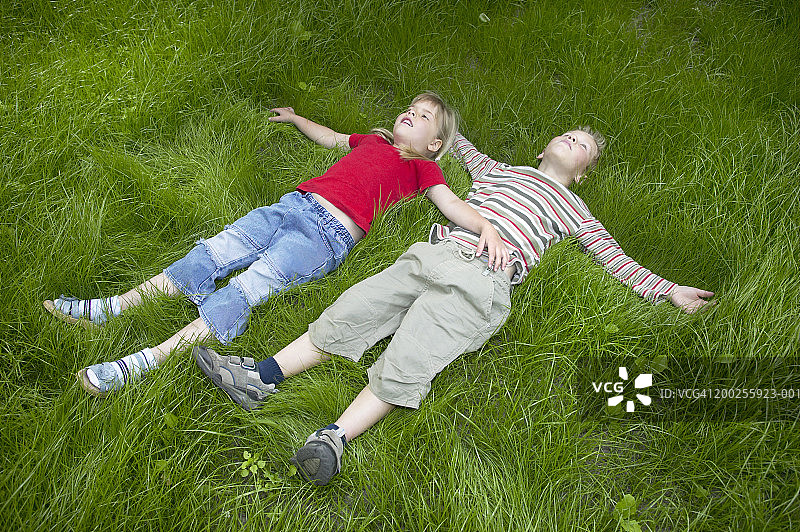 男孩和女孩(4-6)躺在草地上，双臂伸展图片素材
