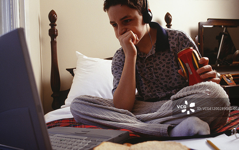16-17岁的男孩坐在床上使用笔记本电脑图片素材