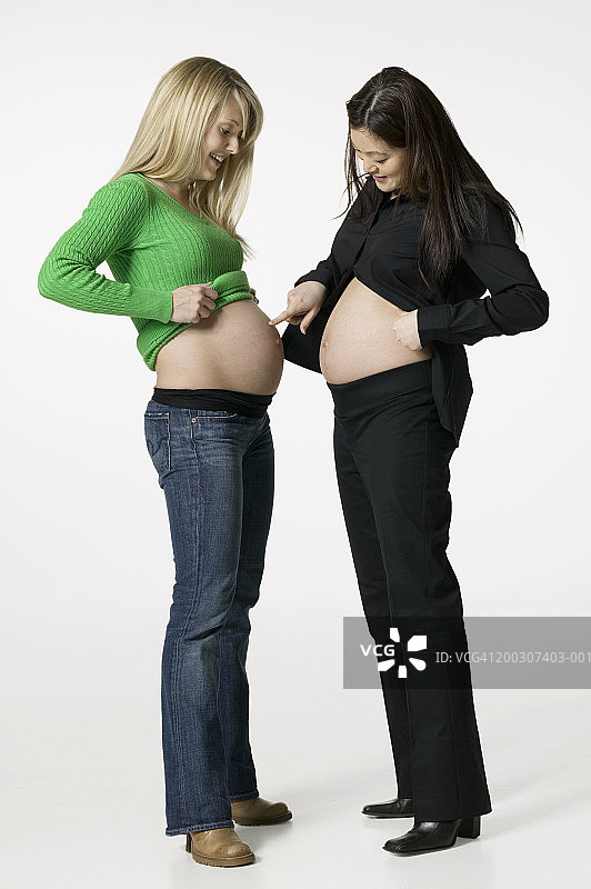 两个孕妇在工作室里比较自己的肚子图片素材
