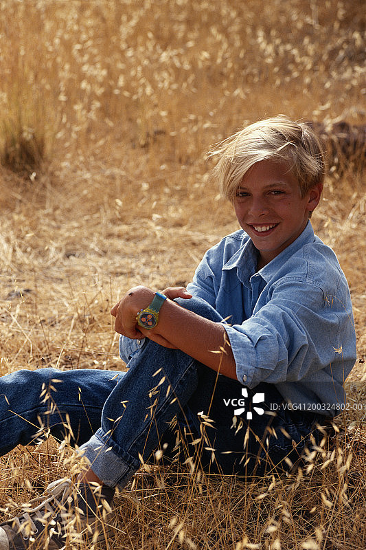 男孩(10-11)坐在田野里，微笑着，肖像图片素材