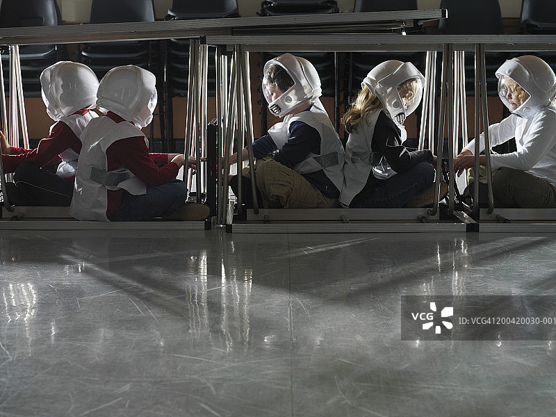 儿童(5-7岁)坐在桌子下的太空人服装，侧视图图片素材