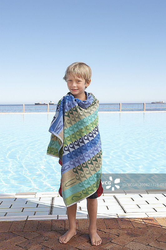 男孩(6-8岁)用毛巾裹在室外游泳池旁，肖像图片素材