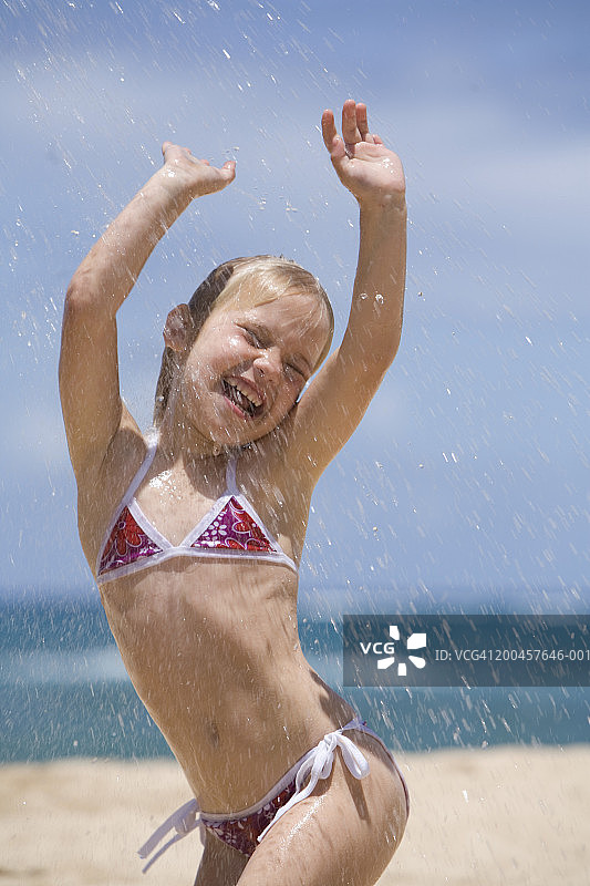 女孩(5-7岁)在沙滩上玩水花，手臂抬起，眼睛闭上图片素材
