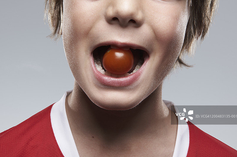 男孩(8-10岁)牙齿间夹着西红柿，特写图片素材