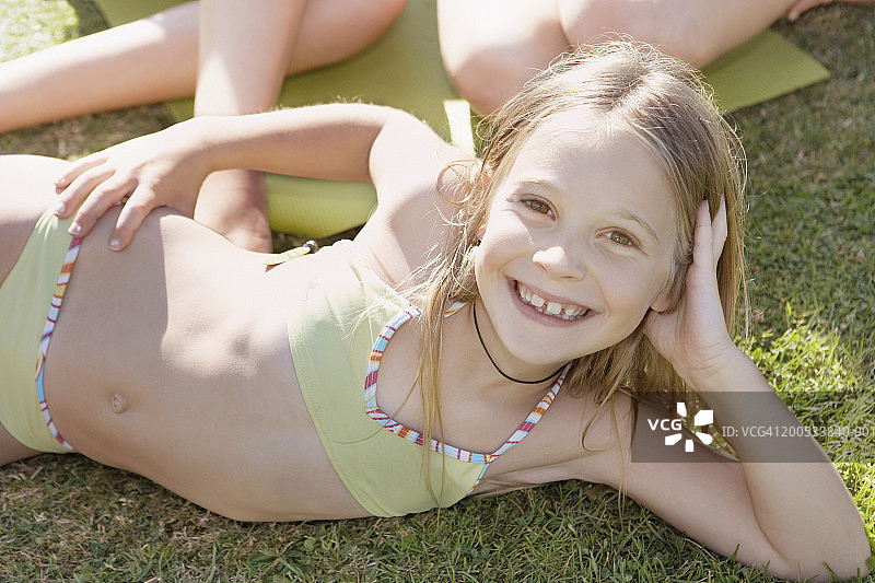 女孩(10-12)躺在草地上的比基尼微笑，肖像图片素材