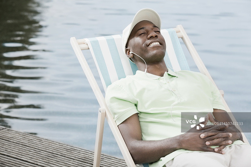 一个戴着耳机在湖边的躺椅上放松的快乐男人图片素材
