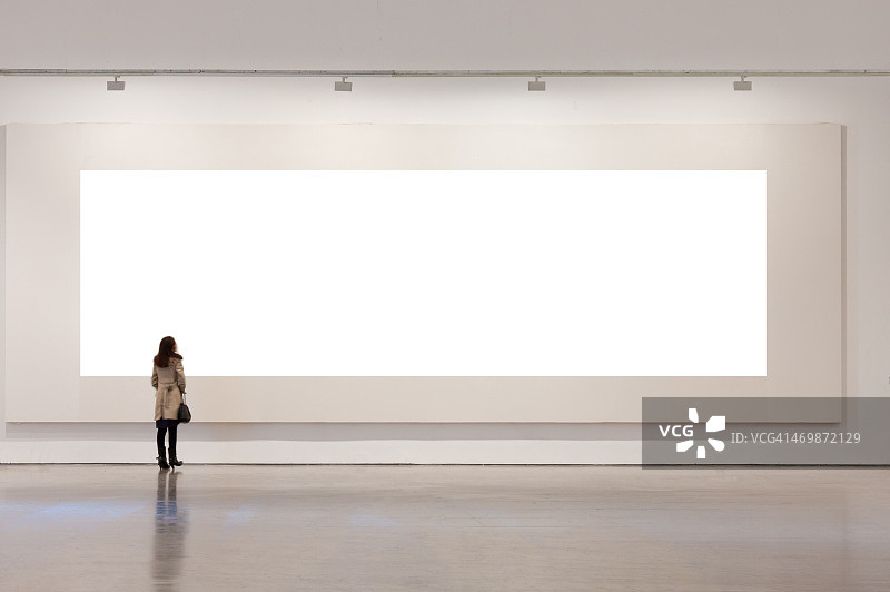 一个女人在画廊里看着白色的画框图片素材