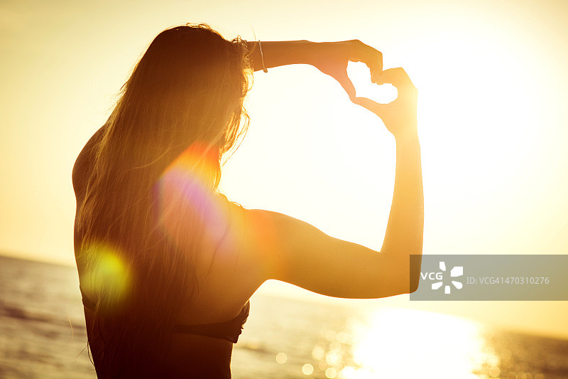 一个女人在海滩上用手做一个心形的象征图片素材