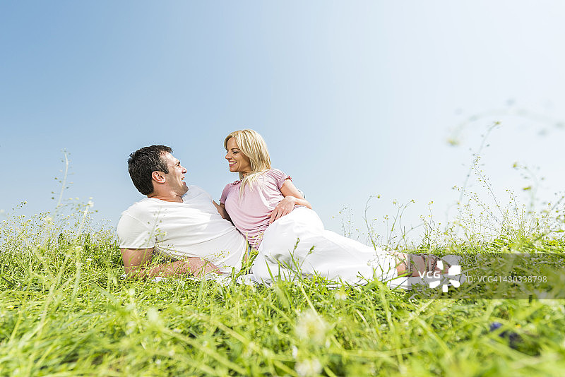 一对恩爱的夫妇坐在草地上互相聊天。图片素材