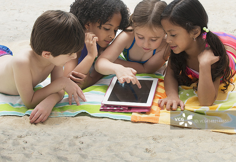 孩子们在沙滩上的毯子上使用数字平板电脑图片素材