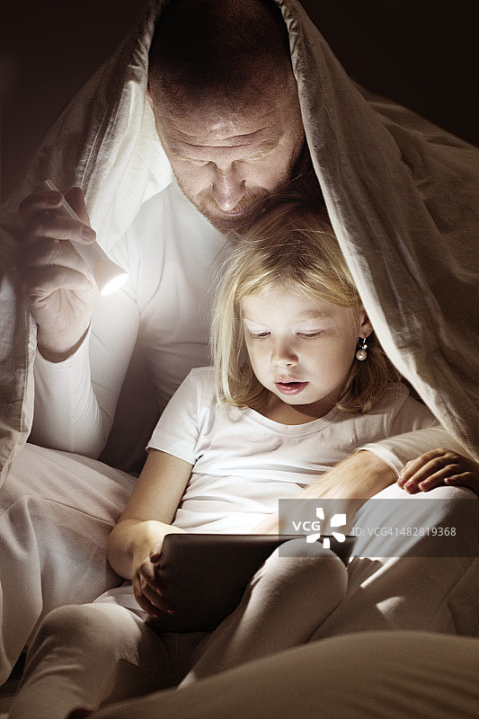 父亲和女儿在睡前使用平板电脑图片素材
