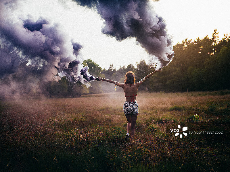 嬉皮女孩带着紫色烟雾在田野里奔跑图片素材