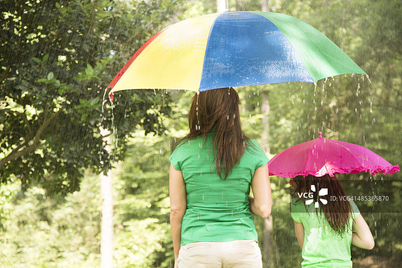 孩子撑着粉红色的伞，妈妈在外面淋雨。夏天。图片素材