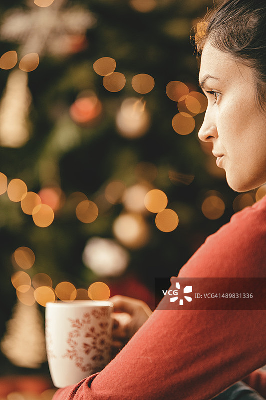 沉思的年轻女子在圣诞树旁喝茶图片素材