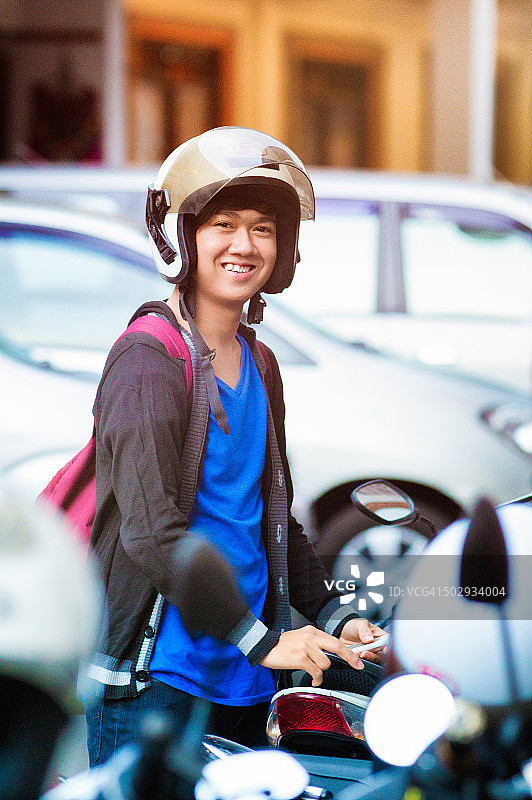 微笑的男性印尼少年肖像在停车场与头盔图片素材