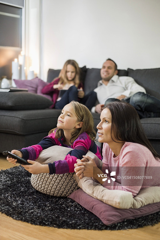 母亲和女儿在地板上看电视，背景是家人图片素材