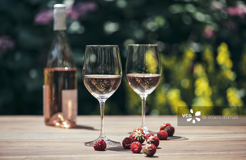 两杯玫瑰酒，酒瓶，草莓和覆盆子放在木桌上图片素材