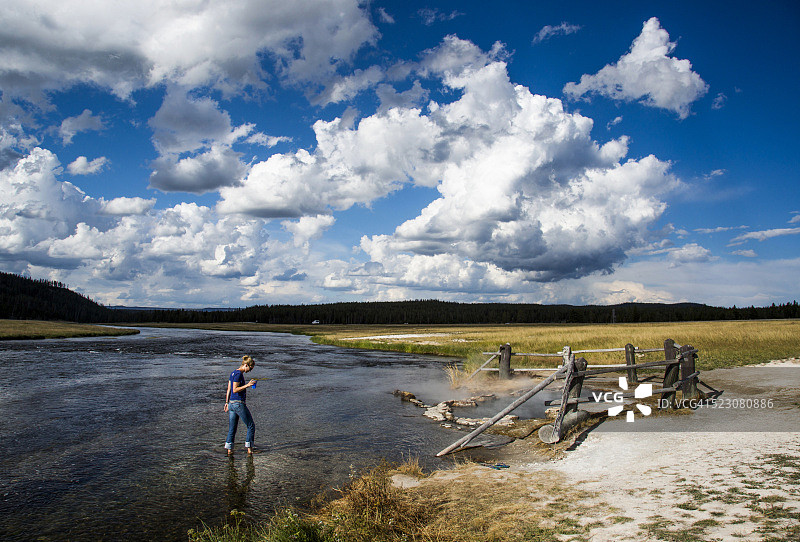 美国怀俄明州黄石国家公园，一名年轻女子涉水穿过一条浅河图片素材
