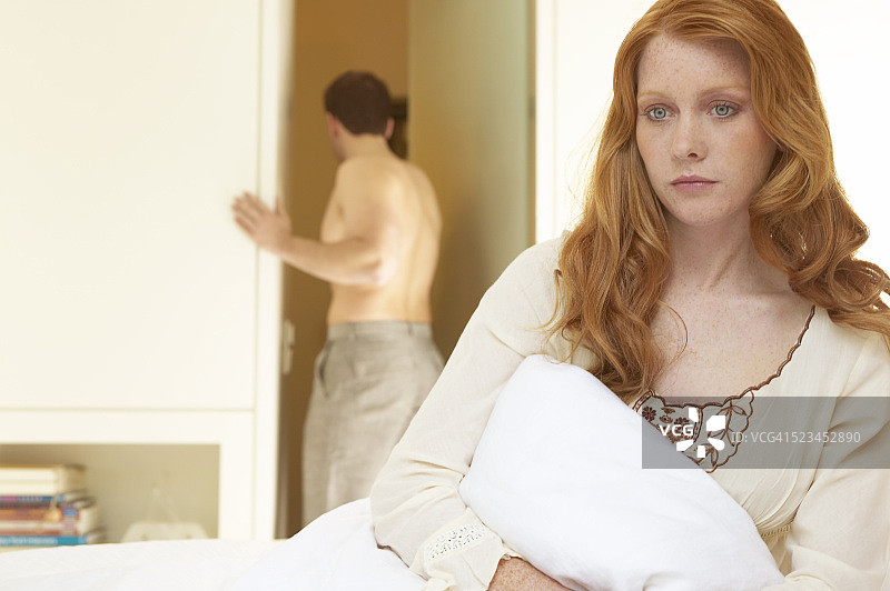 女人在床上，看着关心而丈夫进入浴室在背景图片素材