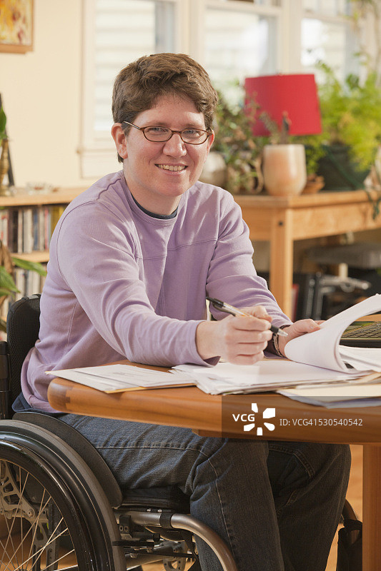 患有多发性硬化症的女商人坐在轮椅上在家做文书工作图片素材