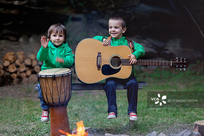 两个可爱的男孩，在篝火旁演奏乐器图片素材