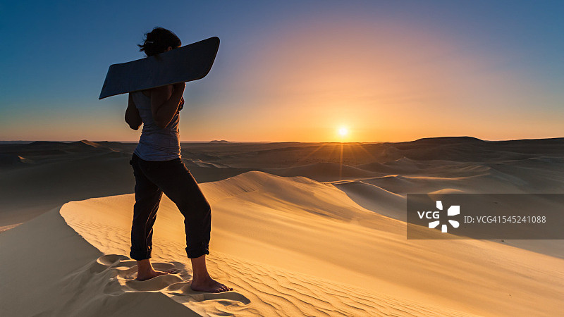 一名年轻女子在非洲撒哈拉沙漠日落时滑沙图片素材