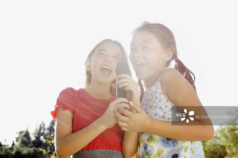 两个微笑的女孩(10-12)在室外对着麦克风唱歌图片素材