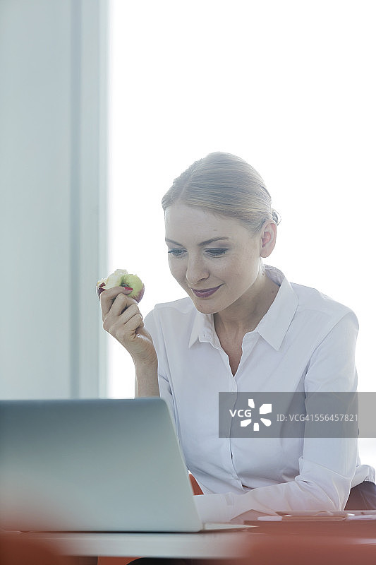 女商人坐在办公桌前吃苹果图片素材