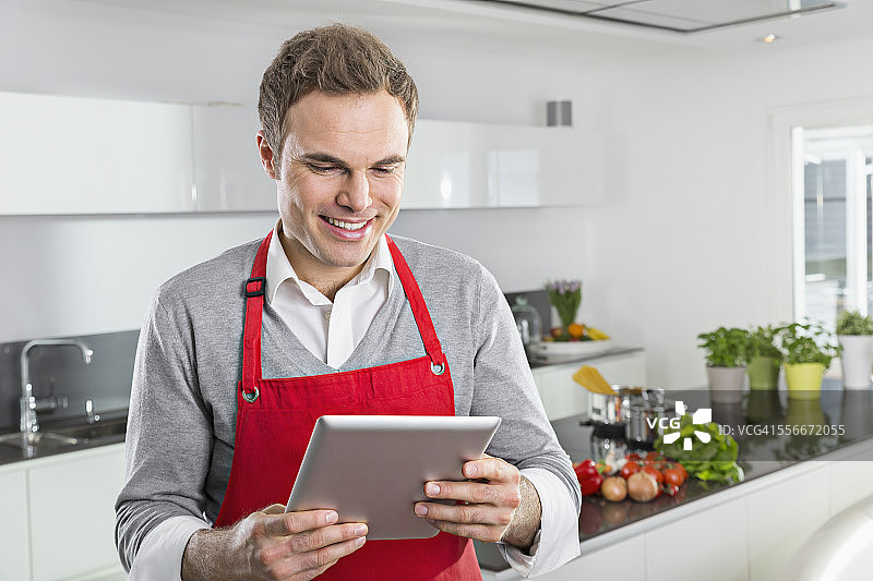 微笑的男人看数字平板电脑在厨房图片素材