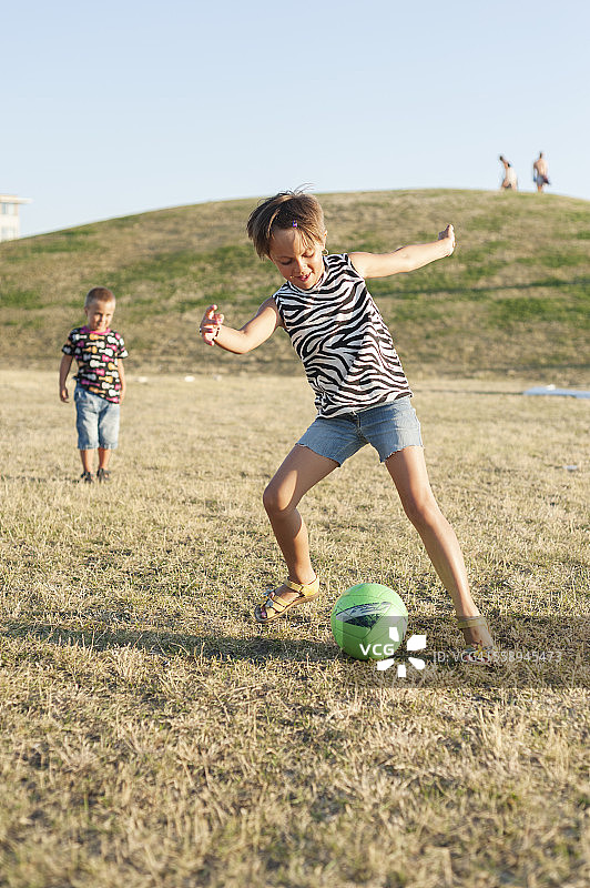 小女孩在草地上踢球，哥哥看着她图片素材